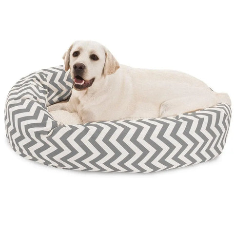 A yellow Labrador retriever relaxes contently on the Majestic Pet Chevron Sherpa Bagel Dog Bed, featuring a gray and white zigzag design and water-resistant, outdoor-treated polyester fabric for spine support.