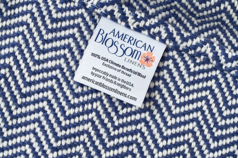 A close-up of an American Blossom Linens label on a Chevron Pattern Soft Wool Throw Size Blanket, showing its made in the USA from 100% Climate Beneficial wool, and lists americanblossomlinens.com.