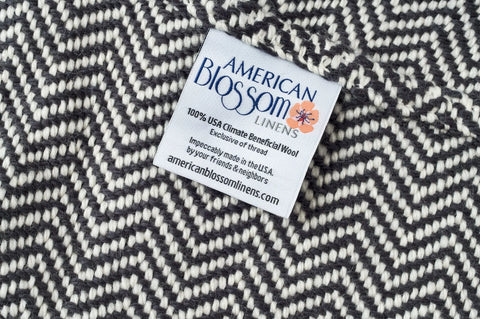 A close-up of the Chevron Pattern Soft Wool Throw Size Blanket by American Blossom Linens, showing its black and white chevron weave and a fabric label with care details.