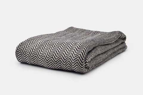 The American Blossom Linens Chevron Pattern Soft Wool Throw Size Blanket, featuring a black and white chevron design, is showcased neatly folded against a plain white background.