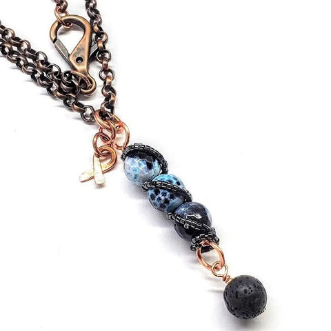 The Alexa Martha Designs Child Abuse Prevention Awareness Beaded Gemstone Stick Pendant With Lava Rock Bead Charm Necklace features a handmade dark metal chain, marbled black, blue, and white gemstone beads, and a lobster clasp closure.