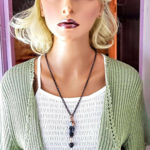 A mannequin with blonde hair wears dark lipstick, a light green knit cardigan over a white textured top, and the Alexa Martha Designs Child Abuse Prevention Awareness Beaded Gemstone Stick Pendant With Lava Rock Bead Charm Necklace, against a pastel background.