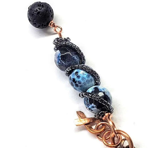 The Child Abuse Prevention Awareness Beaded Gemstone Stick Pendant Necklace by Alexa Martha Designs features three blue marbled beads wrapped in black wire, a textured lava rock essential oil bead topper, copper wire, and decorative copper accents.