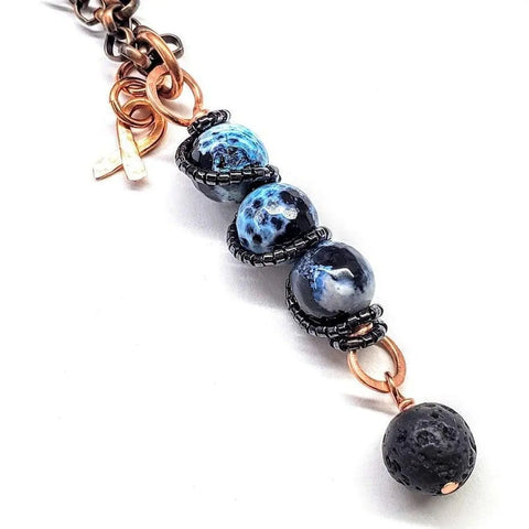 The Alexa Martha Designs Child Abuse Prevention Awareness Beaded Gemstone Stick Pendant Necklace features three marbled blue and black beads, a lava rock charm bead, copper rings, and a small copper charm on a white background.