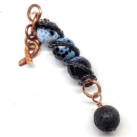 The Alexa Martha Designs Child Abuse Prevention Awareness Beaded Gemstone Stick Pendant Necklace features three blue marbled beads wrapped in black wire, a lava rock bead charm, copper rings, and a toggle clasp—perfect for essential oils.