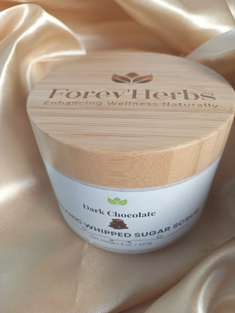 A round jar of Forev'Herbs Chocolate Delight Organic Whipped Sugar Scrub with a bamboo lid rests on shiny beige satin, naturally enhancing wellness as it gently exfoliates your skin.