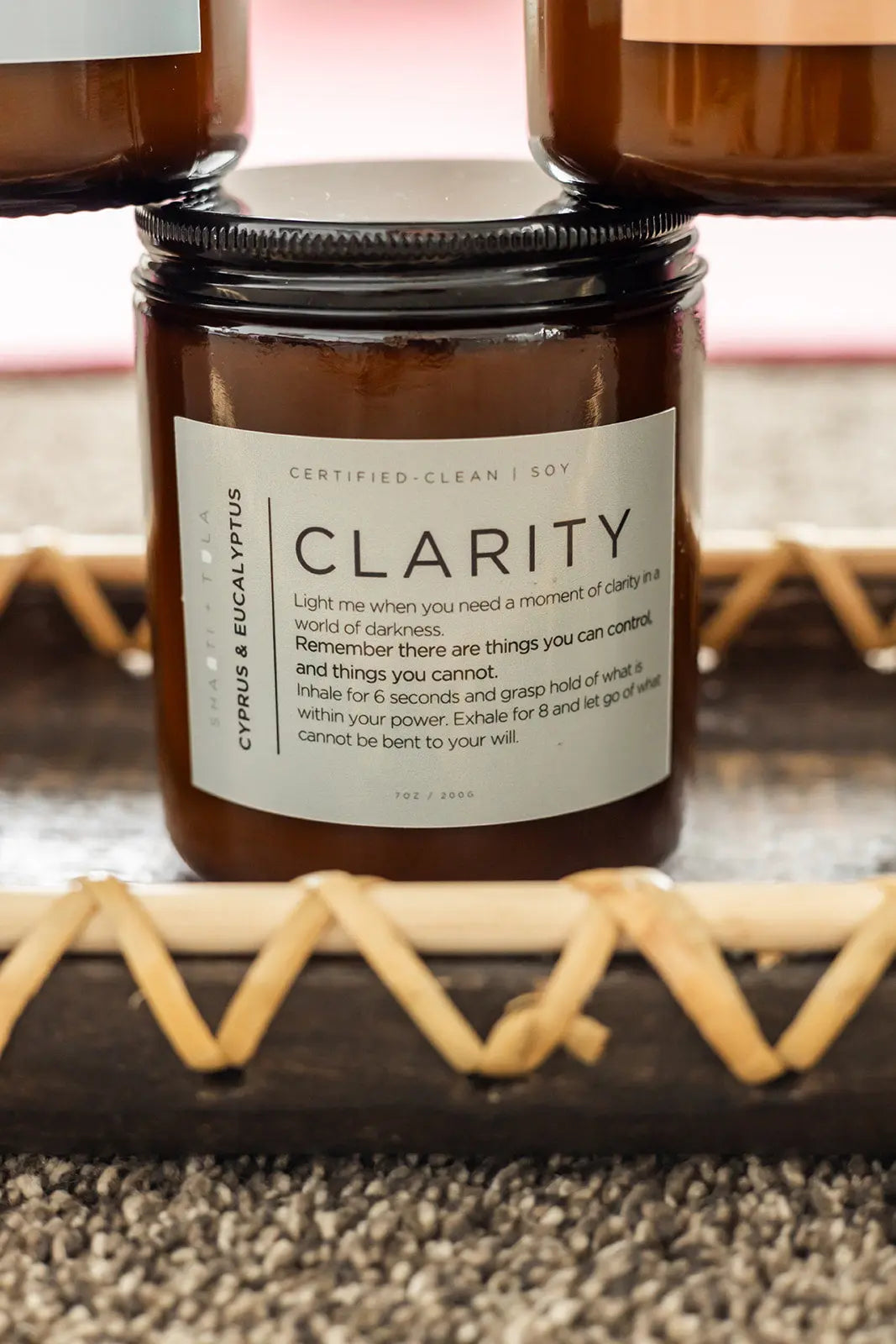 A brown glass Clarity – Cypress & Eucalyptus Soy Candle by Shanti + Tula rests on a wooden tray, its label featuring a relaxation ritual and guidance for finding clarity and letting go. Clean-burning, USA-made wellness candle.