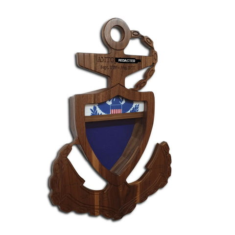The Coast Guard Chief Petty Officer (CPO) Anchor Shadow Box by Legacies of America Woodworking Company features a wooden anchor-shaped plaque with a shield, eagle, red building on top, and blank blue display area. Crafted from real hardwoods, some engraved text is partially redacted.