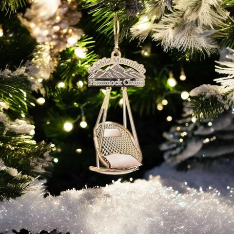 A close-up of a Christmas tree with white lights and snow-dusted branches displays a Cobble Mountain Keepsake Ornament - 1st Edition by Cobble Mountain, adding handcrafted charm to the festive holiday decor.