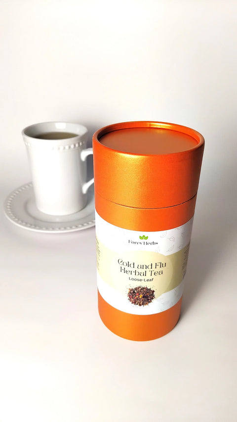 An orange cylindrical Forev'Herbs Cold and Flu Herbal Tea container sits in front of a white cup and saucer, highlighting this immune-boosting loose-leaf tea against a plain white background.