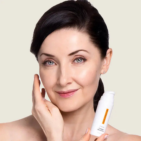 A woman with fair skin and dark hair smiles, touching her cheek while holding Open Formulas Collagen Peptide Moisturizer, showcasing its peptide benefits for smoother skin against a light background.