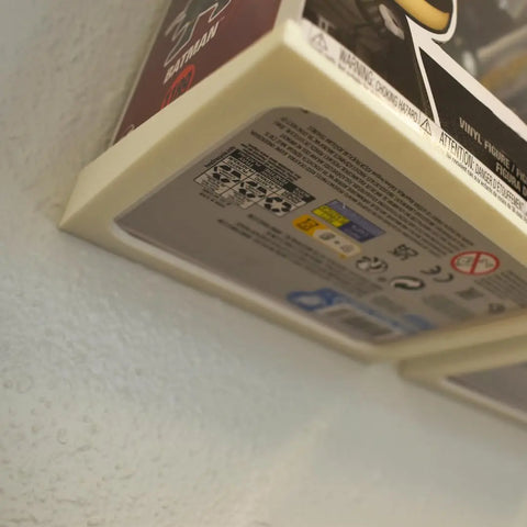 A close-up of two Funko Pop figure boxes mounted on textured white wall using Chatelet Manufacturings Collectible Wall Display Stands—perfect for displaying original figures with boxes. Made in USA and compatible with Funko Pop figures in box.