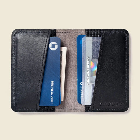 The CASUPO Compact Bifold With RFID Protection - Black Limited Edition is open, showing several cards inside—including a blue business debit card and an American Express—against a light background.