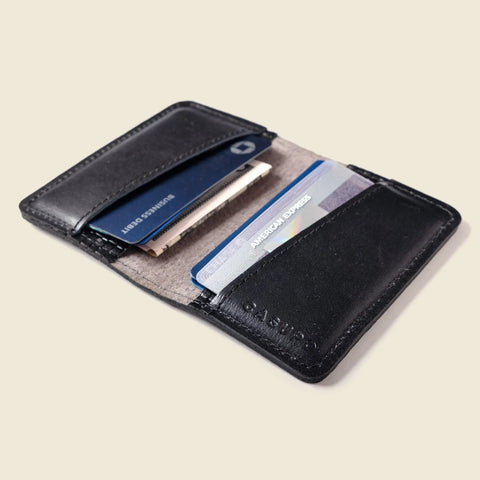 The CASUPO Compact Bifold With RFID Protection - Black Limited Edition is shown open on a light beige surface, displaying several credit cards, including an American Express card, and paper items in its two pockets.