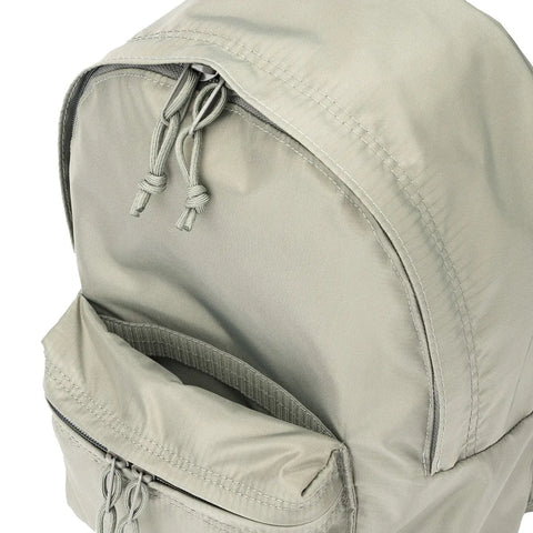 A close-up of the MIS Daypack S - Foliage shows its light gray, water-resistant nylon fabric, adjustable shoulder straps, two zipper pulls on the main compartment, and an open front pocket.