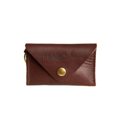 The Urban Southern Keychain Coin Purse is a small brown full-grain leather pouch with a brass button closure and Urban Southern embossed on the front, displayed against a white background.