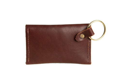 The Urban Southern Keychain Coin Purse is a small brown full-grain leather pouch with a brass keyring on one corner, attached by a leather strap and metal rivet, displayed on a white background.