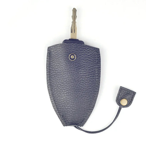 A metallic key is partly covered by a Rogue Industries Rogue Leather Key Protective Case in textured dark gray leather with a snap button, while the detached flap lies nearby.
