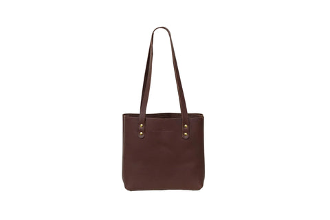 The Mini Urban Tote by Urban Southern is a dark brown leather handbag with two long handles and gold rivet accents, made in America and shown against a white background.