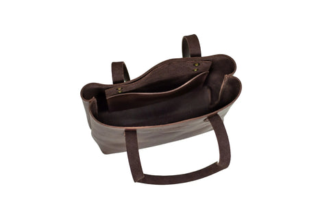 The Mini Urban Tote by Urban Southern is shown from above on a white background. This brown luxury leather tote features two handles, a spacious main compartment, and an inner pocket with a snap button closure.