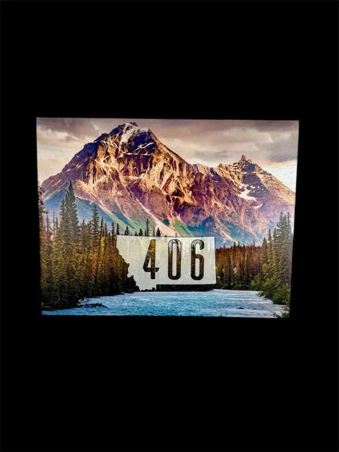 A scenic photo of snowy mountain peaks, pine trees, and a river features a Montana-shaped 406 sign. A B. James Design & Woodwork Regular Size Concealment Cabinet with Enhanced Security is displayed on a black background.