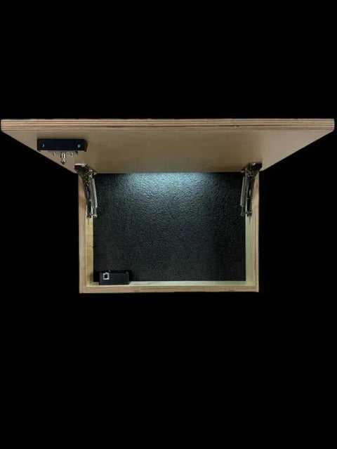 The Regular Size Concealment Cabinet by B. James Design & Woodwork is shown open from above, featuring a hinged lid, dark customizable interior with metal hinges, and a mounted black electronic device against a solid black background.