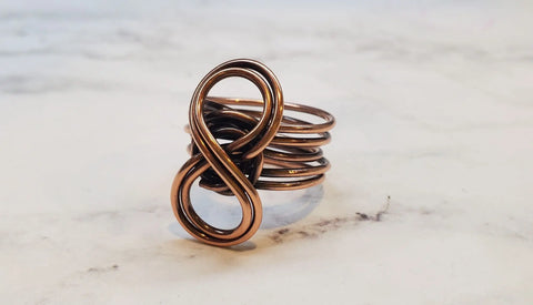 The Copper Eternity Ring by Alexa Martha from Alexa Martha Designs, featuring a handmade infinity symbol design, rests on a white marble surface.