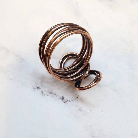 The Copper Eternity Ring by Alexa Martha from Alexa Martha Designs, featuring handmade copper rings of various sizes, is elegantly displayed on a white marble surface.