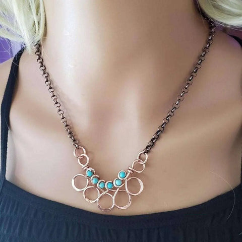 A close-up of a person wearing the Alexa Martha Designs “As Seen on Ashley Liao” Copper Turquoise Wire Wrapped Necklace, styled with a black sleeveless square-neck top.