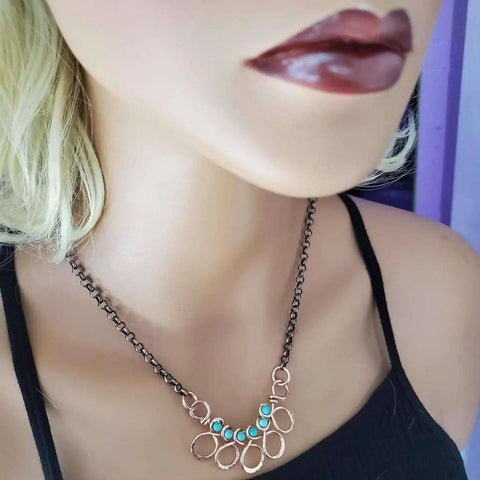 A mannequin models the Alexa Martha Designs As Seen on Ashley Liao necklace—a handcrafted copper turquoise wire-wrapped piece with a bronze chain and blue and white stones, focusing on the necklace and lower half of the face.