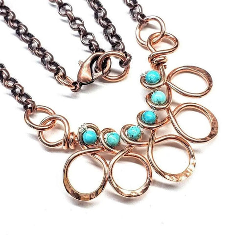 The As Seen on Ashley Liao Copper Turquoise Wire Wrapped Necklace by Alexa Martha Designs features a dark metal chain, hammered copper loops, and four turquoise jasper gemstones, finished with a large lobster clasp for easy wear.