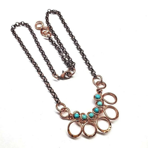 The As Seen on Ashley Liao Copper Turquoise Wire Wrapped Necklace by Alexa Martha Designs features five small turquoise beads among swirling copper loops on a copper chain, shown against a white background.