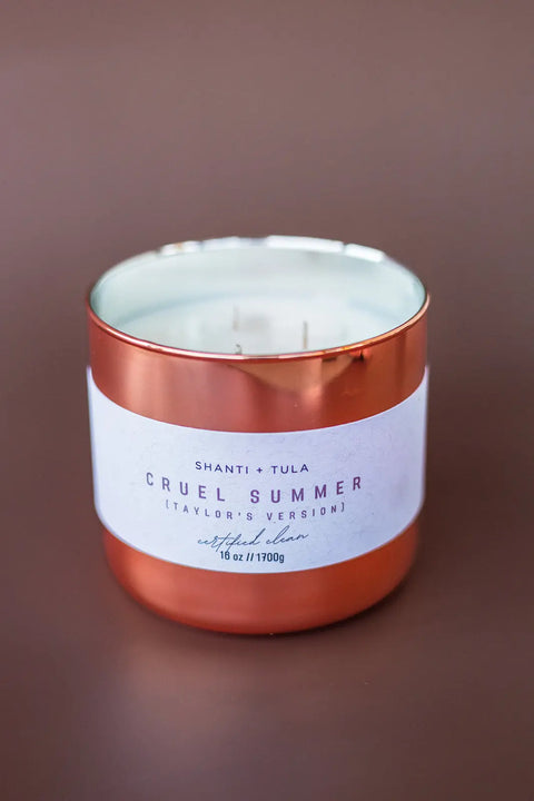 A Copper Vessel 3-Wick Soy Candle by Shanti + Tula, featuring clean-burning soy and a white Cruel Summer (Taylor’s Version) Artificial Dawn label, is shown against a plain brown background. Luxury, USA-made, and gift-ready decor. 16 oz // 1700g.