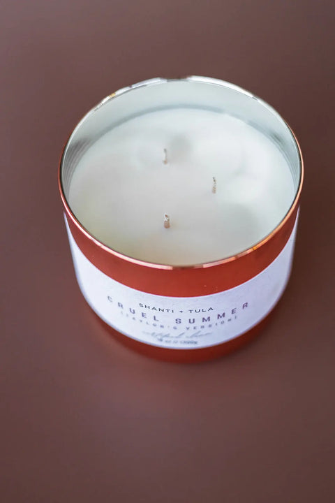 A Copper Vessel 3-Wick Soy Candle by Shanti + Tula, clean-burning and USA-made, sits on a brown surface in a round tin with a red rim. The luxury candle offers exceptional fragrance and gift-ready decor.