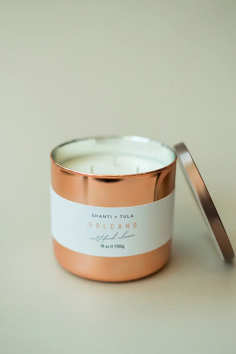 A Shanti + Tula Copper Vessel 3-Wick Soy Candle with a white label sits on a light surface. Its lid is off, revealing white wax and wicks—luxury, clean-burning decor that’s gift-ready and made in the USA.