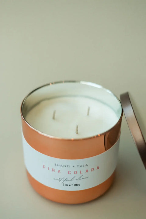 A Shanti + Tula Copper Vessel 3-Wick Soy Candle sits open, its lid off to the side on a light surface, offering clean-burning fragrance and luxury gift-ready decor, all made in the USA.