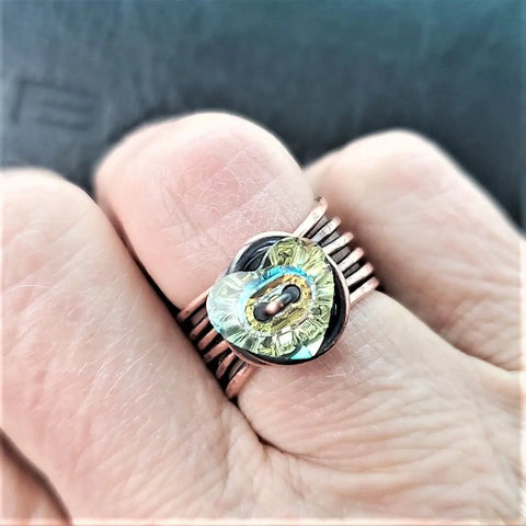 A close-up of a hand wearing the Copper Wire Wrapped Crystal Heart Glam Ring by Alexa Martha Designs, featuring a wire-wrapped crystal heart centerpiece with metallic accents.