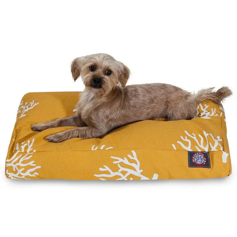 A small light brown dog lies on the Majestic Pet Coral Rectangle Dog Bed in mustard yellow with white coral patterns. This washable bed looks cozy as the alert pup faces the camera.