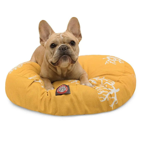 A light brown French Bulldog rests on the Majestic Pet Coral Round Dog Bed, which features a yellow cover with white patterns and a removable design. The dog looks up with perked ears, pictured against a plain white background.