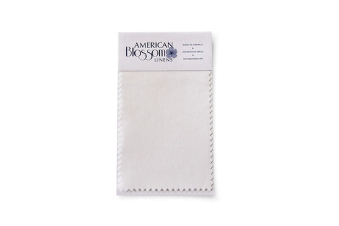 A rectangular USA-grown cotton Swatch with zigzag edges from American Blossom Linens is attached to a branded card featuring printed product details, all displayed on a white background.