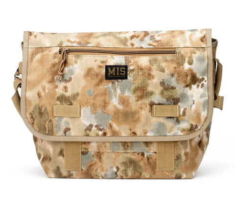 The MIS Messenger Bag - Covert Desert features a tan camouflage Cordura Nylon design with a front zip pocket, adjustable shoulder strap, and brand label on the flap. Made in the USA, its pattern blends brown, tan, and green shades.