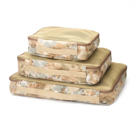 Three rectangular mesh packing cubes in camouflage from MIS are stacked from largest to smallest. The Organizer Set - Covert Desert, made in the USA, keeps your gear tidy and accessible for any adventure.