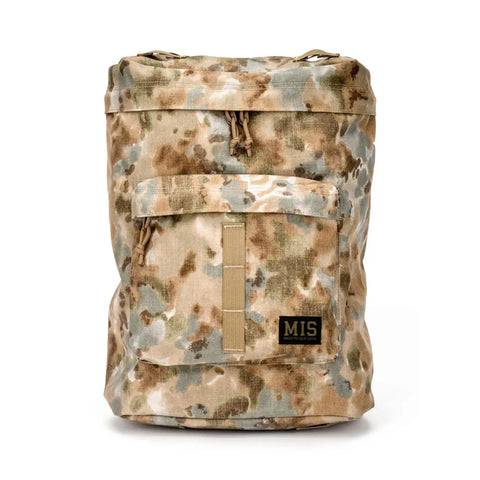 The MIS Backpack - Covert Desert features a tan, brown, and gray camouflage Cordura Nylon design with a front pocket, drawstring closures, padded laptop holder, and an “MIS” logo patch near the bottom. Displayed against a plain white background.
