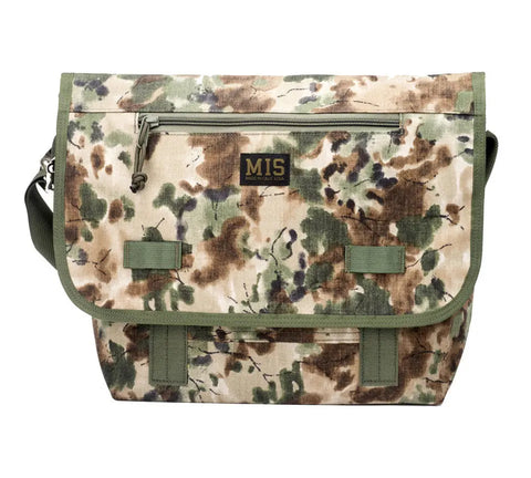 The MIS Messenger Bag - Covert Woodland is made in the USA from camouflage Cordura Nylon, featuring an olive strap, front zipper pocket, flap logo patch, and earthy green, brown, and tan tones for rugged durability.