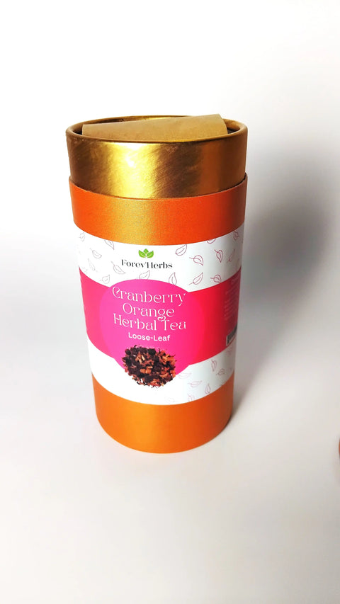 A cylindrical orange container with a gold lid and a pink-and-white label reading "Cranberry Orange Herbal Tea" from Forev'Herbs. This caffeine-free loose-leaf herbal tea is partly open, revealing the inner seal.