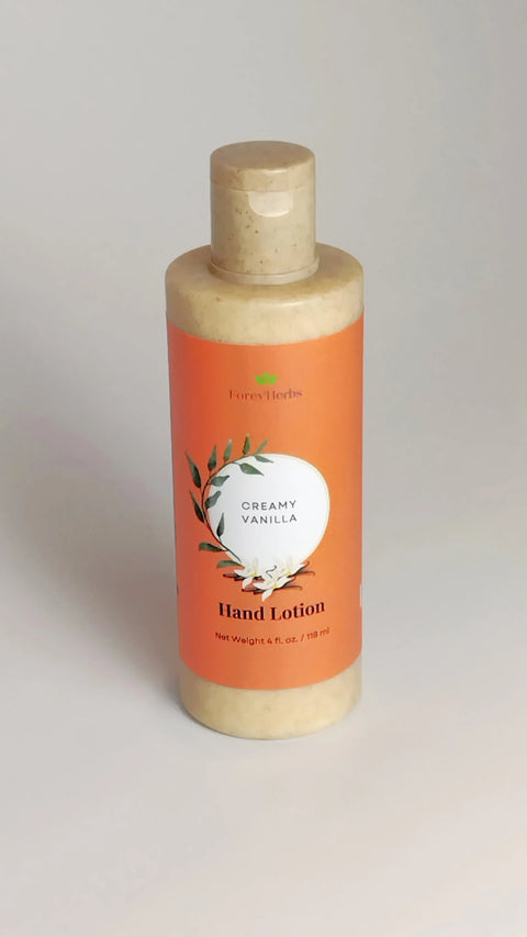 A beige bottle of Forev'Herbs Creamy Vanilla Hand Lotion with an orange label, floral accents, and a flip-top cap stands upright on a light surface—ideal for soothing dry skin.