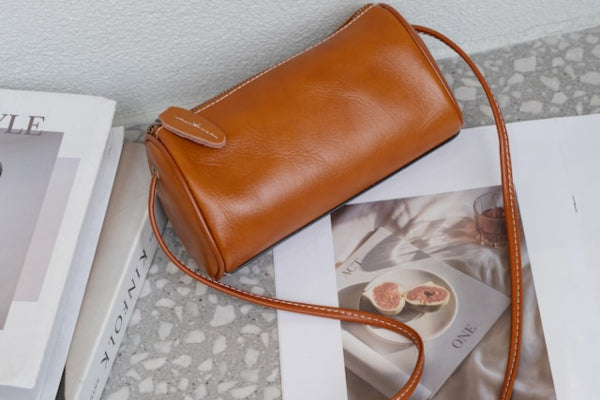 Brown leather handbag on a surface with books and a magazine