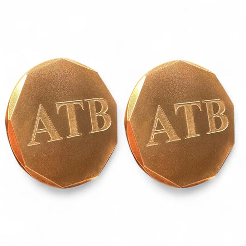 A set of two Personalized Ball Markers by Fairway Reserve, featuring gold-toned, faceted-edge design and engraved uppercase ATB on a white background, offers a sophisticated touch for any golfer.