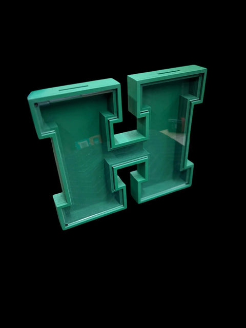 The Letter Piggy Banks by B. James Design & Woodwork feature a green 3D block letter H with a hollow interior and a clear front cover, set against a solid black background—ideal for personalized savings.