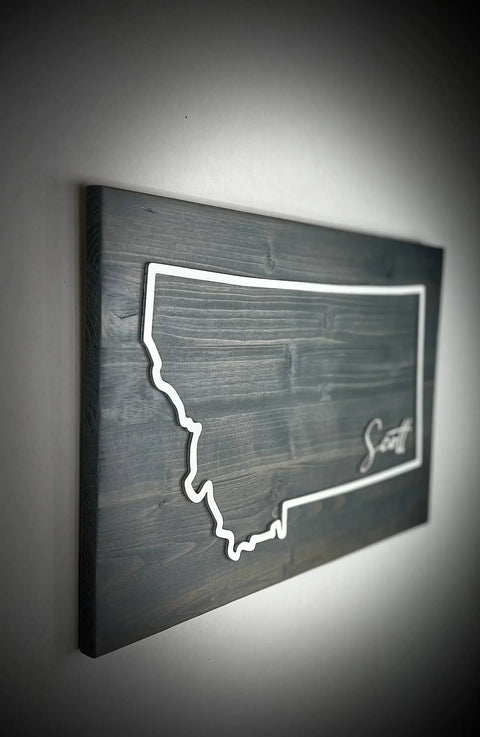 The Large Rectangle Personalized MT Sign by B. James Design & Woodwork features a white outline of Montana with Smith inscribed, mounted on dark wood. Ideal personalized decor for your home—custom colors available.